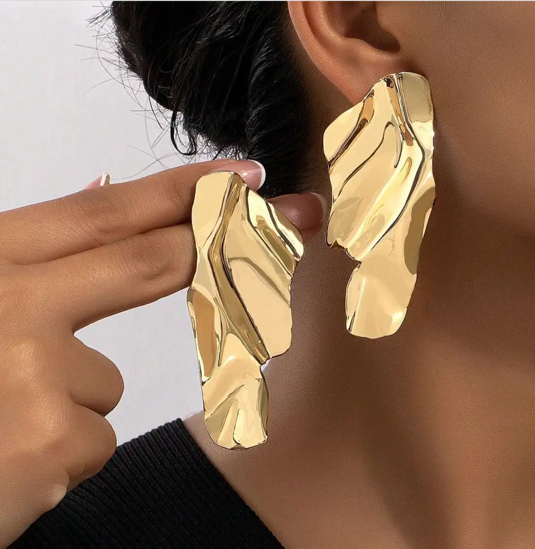 Paire de boucles d'oreilles dorées au design abstrait avec des surfaces ondulées, apportant une touche moderne et artistique.