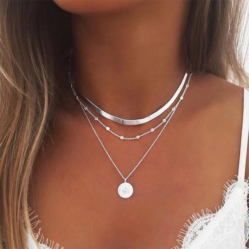 Femme portant trois colliers superposés en argent, avec un ras-du-cou, une chaîne perlée et un pendentif rond.